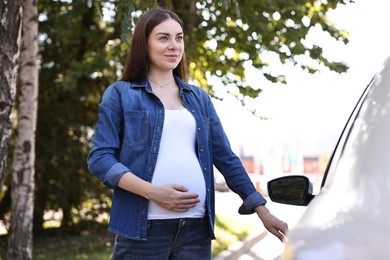 Beautiful pregnant woman opening car door outdoors