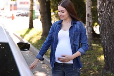 Beautiful pregnant woman opening car door outdoors