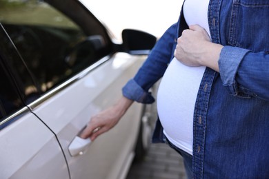 Photo of Pregnant woman opening car door outdoors, closeup