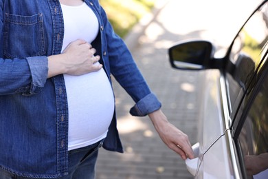 Photo of Pregnant woman opening car door outdoors, closeup