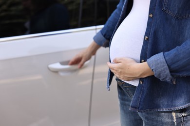 Photo of Pregnant woman opening car door outdoors, closeup