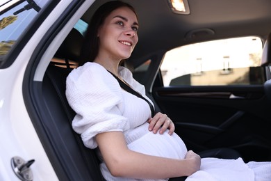 Smiling pregnant woman with safety belt in car