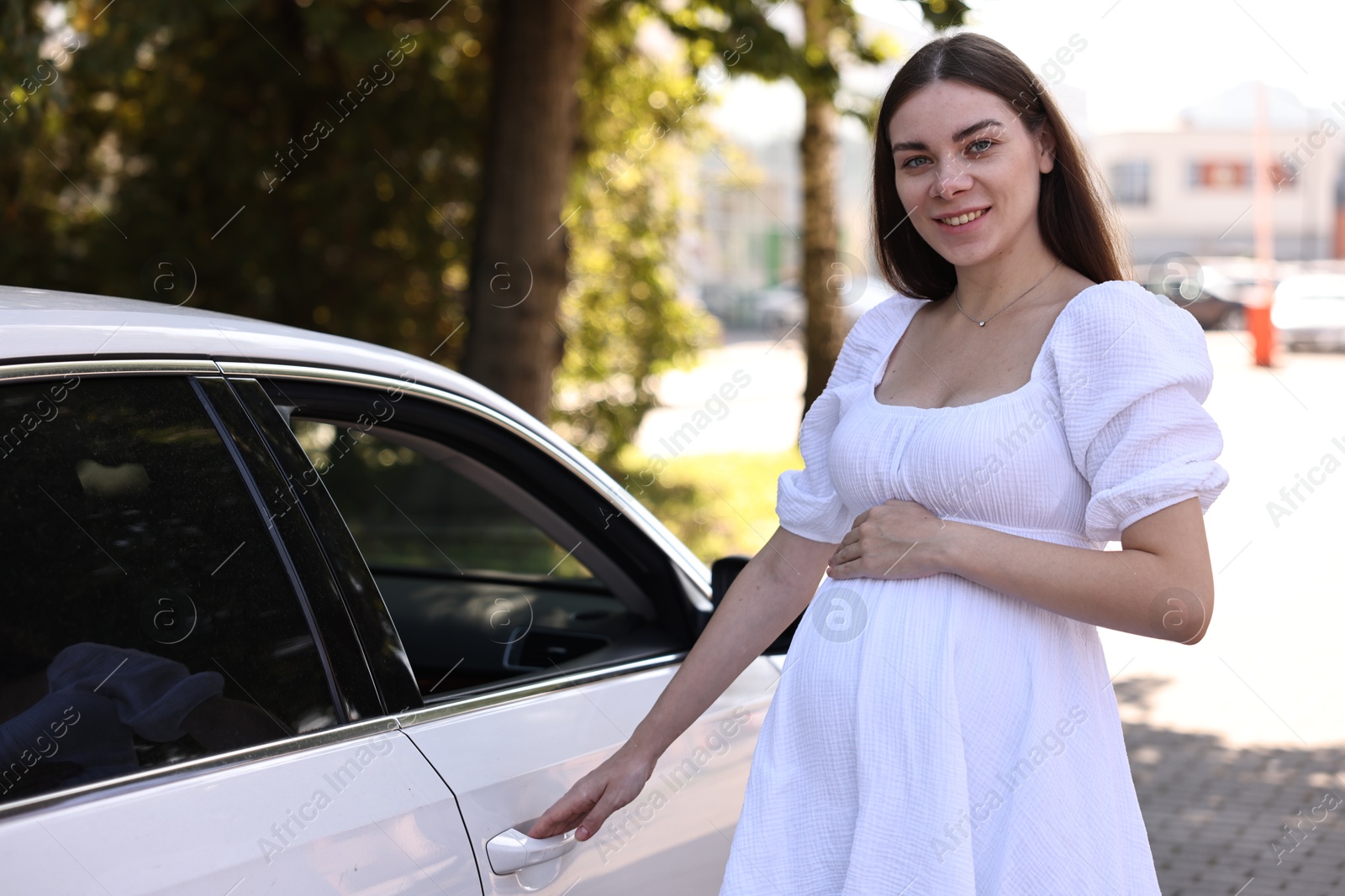 Photo of Portrait of smiling pregnant woman opening car door outdoors