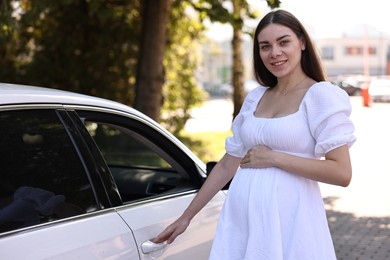 Portrait of smiling pregnant woman opening car door outdoors