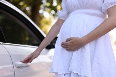 Photo of Pregnant woman opening car door outdoors, closeup