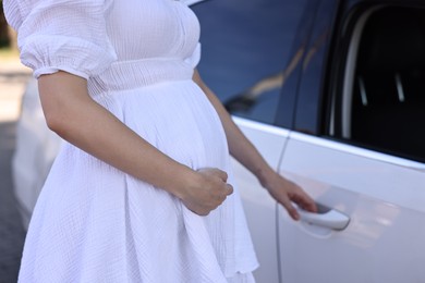 Pregnant woman opening car door outdoors, closeup