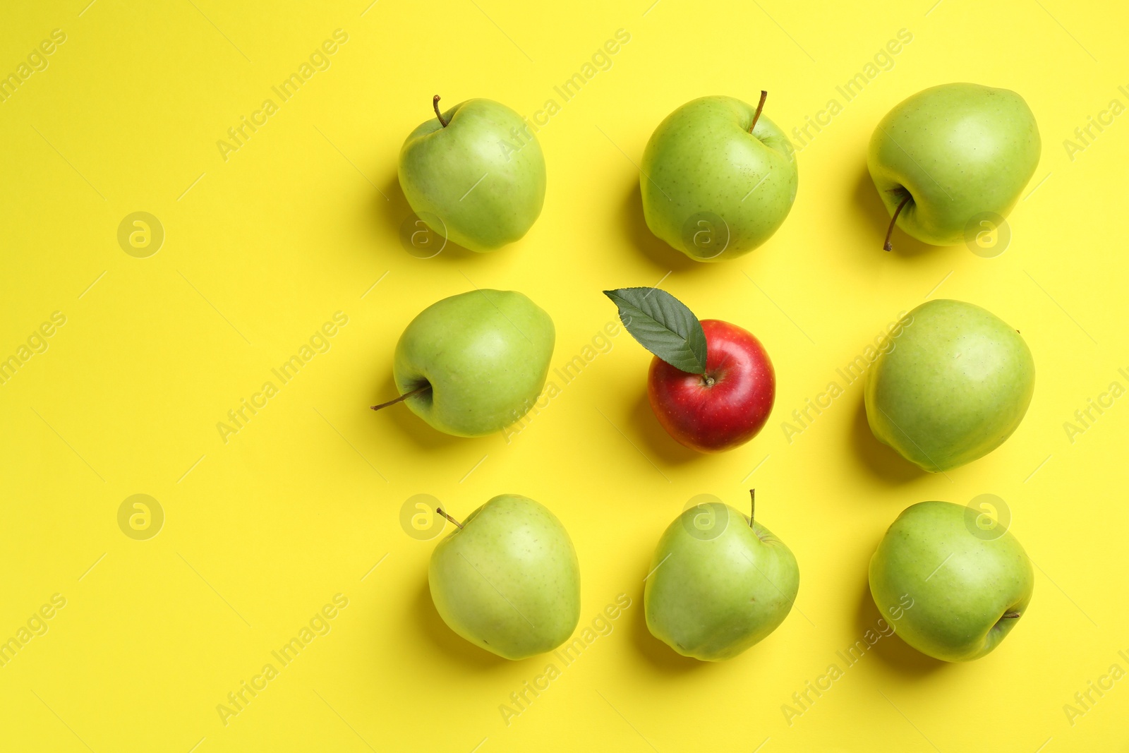 Photo of Flat lay composition with red apple surrounded by green ones on yellow background. Space for text