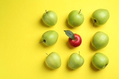 Flat lay composition with red apple surrounded by green ones on yellow background. Space for text