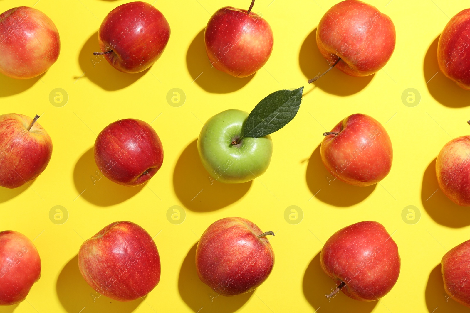 Photo of Flat lay composition with green apple surrounded by red ones on yellow background