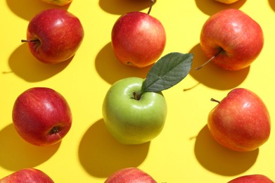 Photo of Green apple surrounded by red ones on yellow background, above view