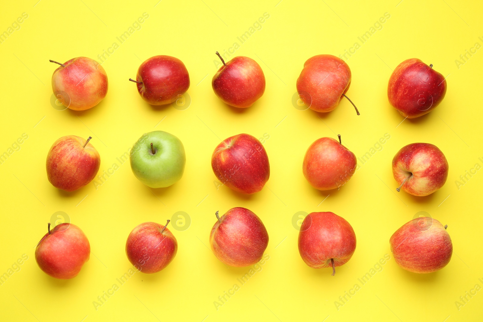 Photo of Flat lay composition with green apple surrounded by red ones on yellow background