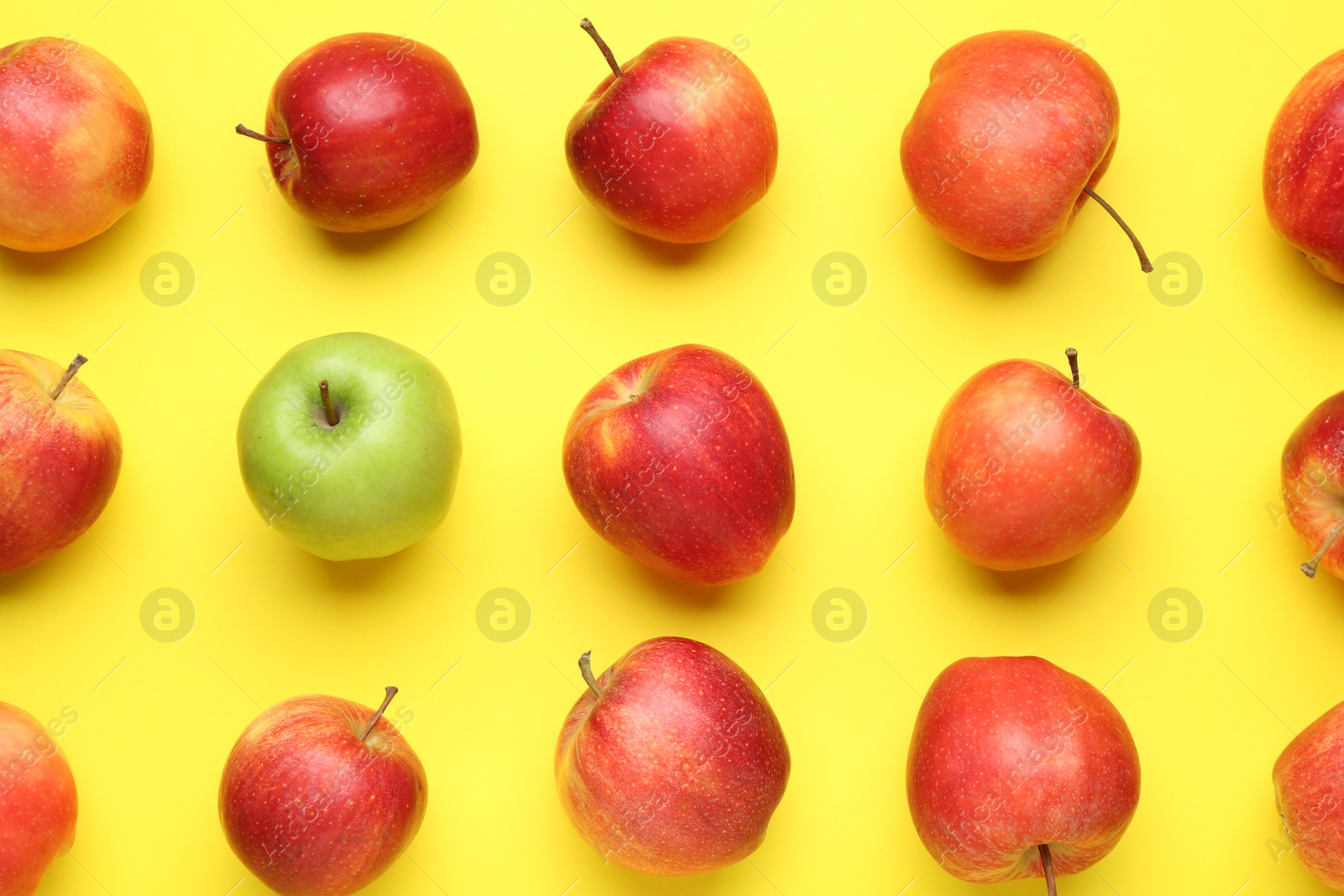 Photo of Flat lay composition with green apple surrounded by red ones on yellow background