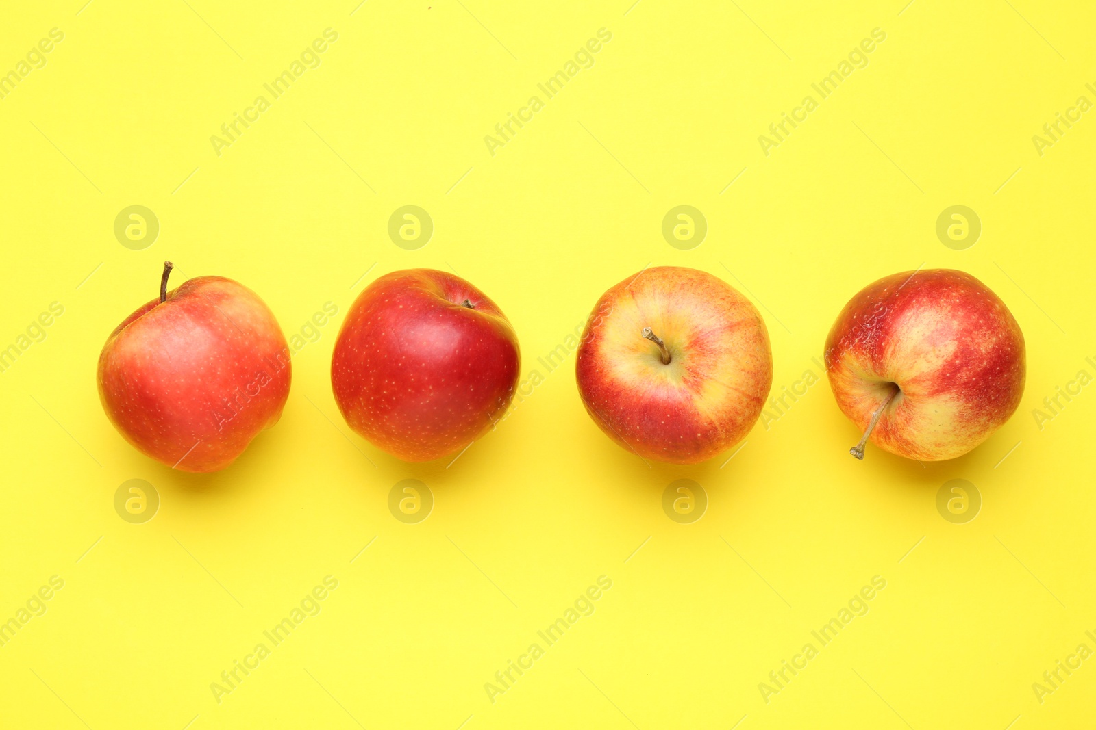 Photo of Red apples on yellow background, flat lay