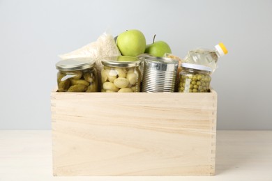 Photo of Different food products for donation in wooden crate on table against grey background