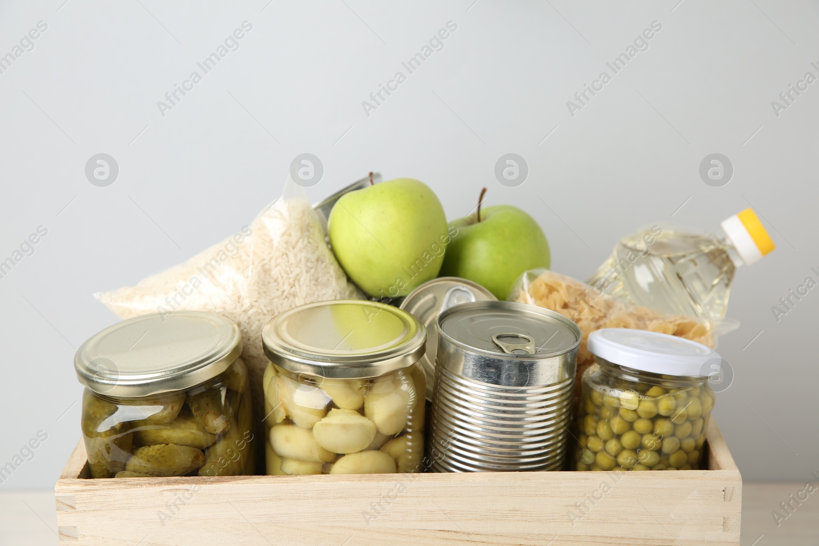 Photo of Different food products for donation in wooden crate on grey background, closeup