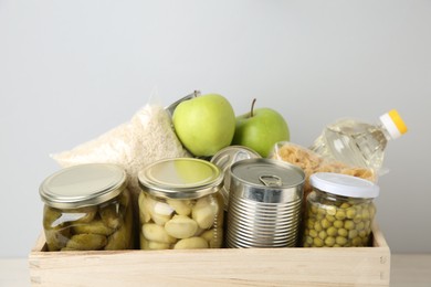 Photo of Different food products for donation in wooden crate on grey background, closeup