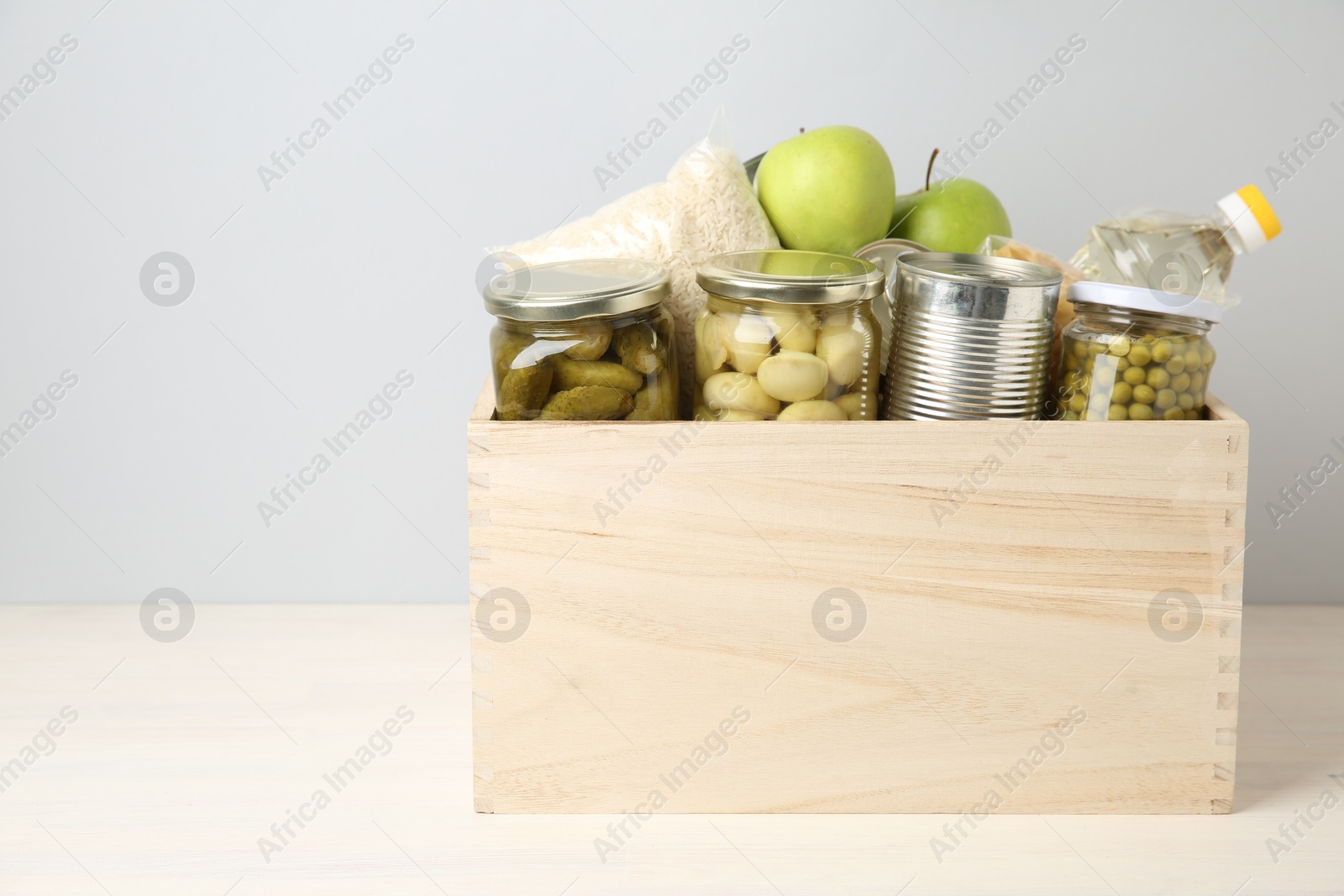 Photo of Different food products for donation in wooden crate on table against grey background, space for text