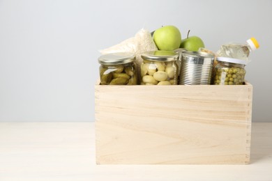 Photo of Different food products for donation in wooden crate on table against grey background, space for text