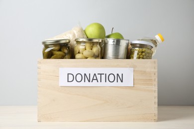 Photo of Different food products for donation in wooden crate on table against grey background