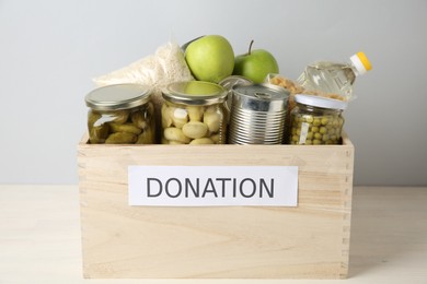 Photo of Different food products for donation in wooden crate on table against grey background