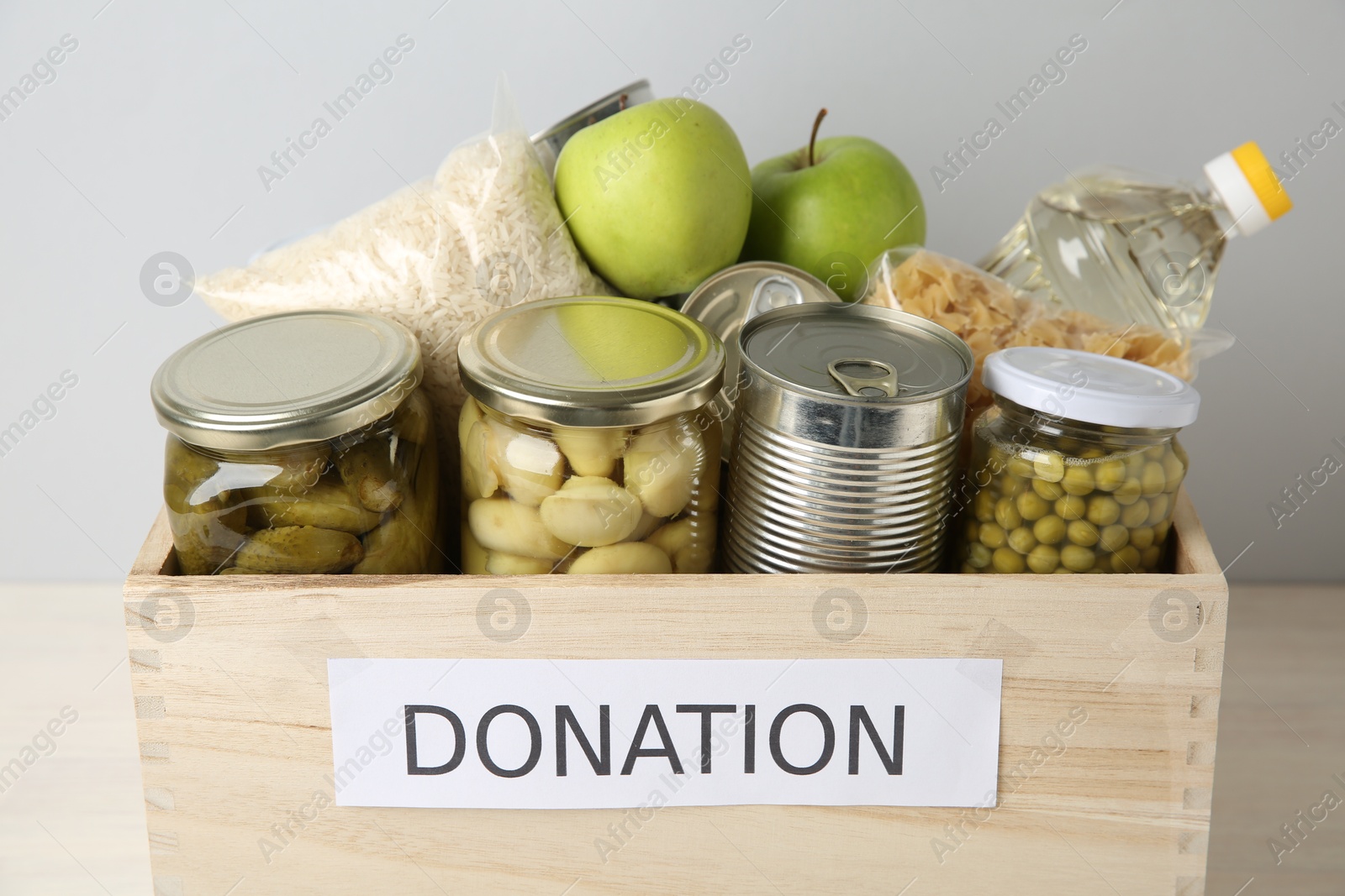 Photo of Different food products for donation in wooden crate on table, closeup