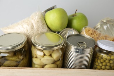 Photo of Different food products for donation in wooden crate on grey background, closeup