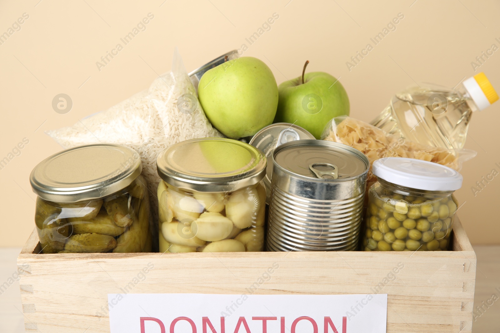 Photo of Different food products for donation in wooden crate on beige background, closeup