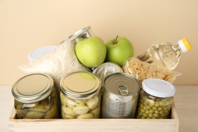 Photo of Different food products for donation in wooden crate on table, closeup