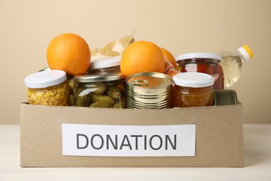 Photo of Different food products for donation in box on table against beige background