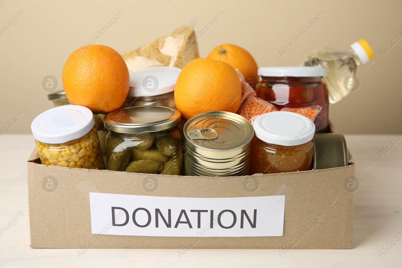 Photo of Different food products for donation in box on table against beige background