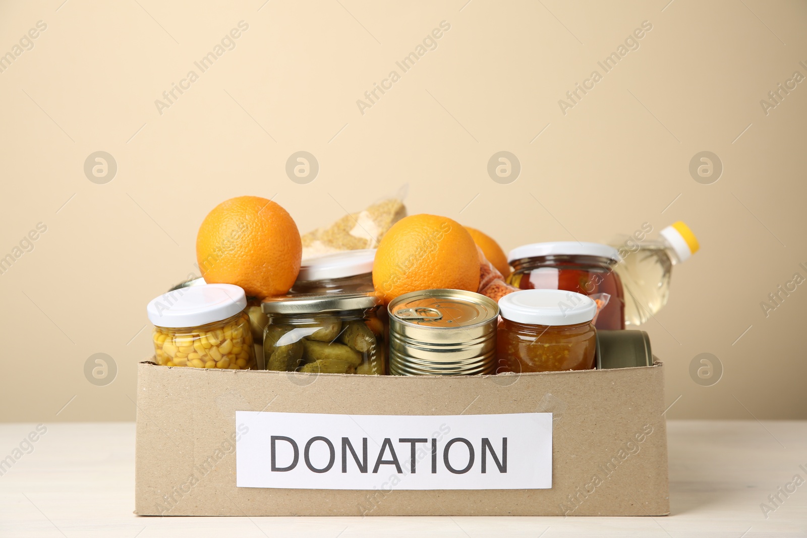 Photo of Different food products for donation in box on table against beige background