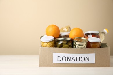 Photo of Different food products for donation in box on table against beige background, space for text