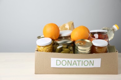 Photo of Different food products for donation in box on table against grey background