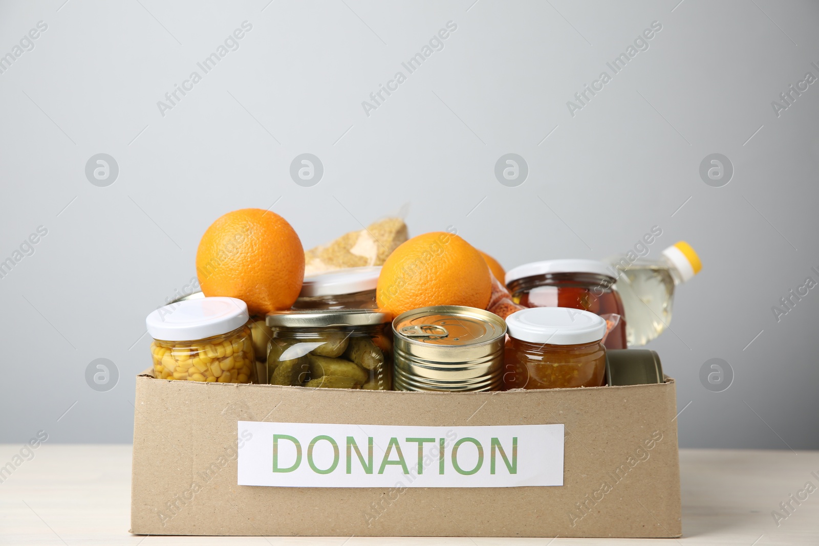 Photo of Different food products for donation in box on table against grey background