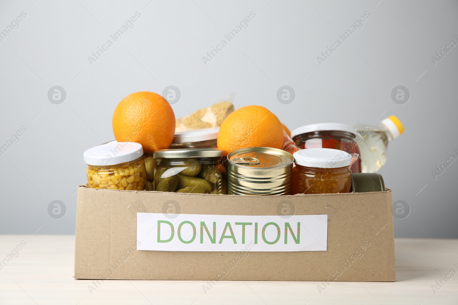 Photo of Different food products for donation in box on table against grey background