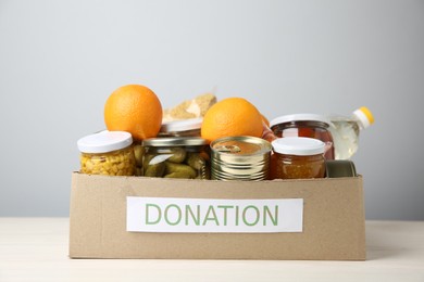 Photo of Different food products for donation in box on table against grey background