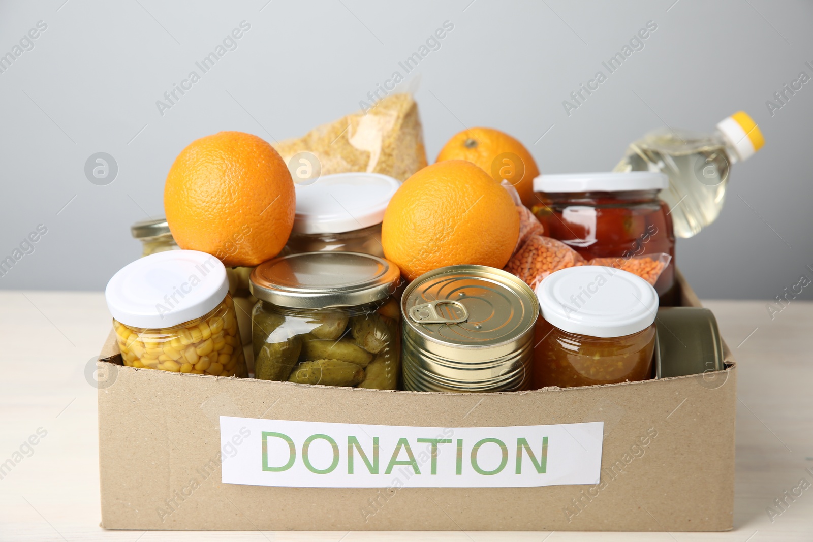 Photo of Different food products for donation in box on table against grey background