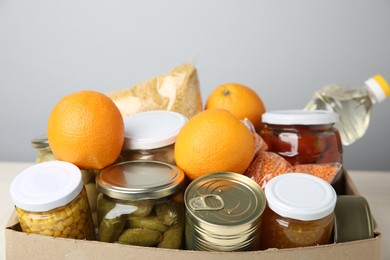 Photo of Different food products for donation in box on table against grey background, closeup