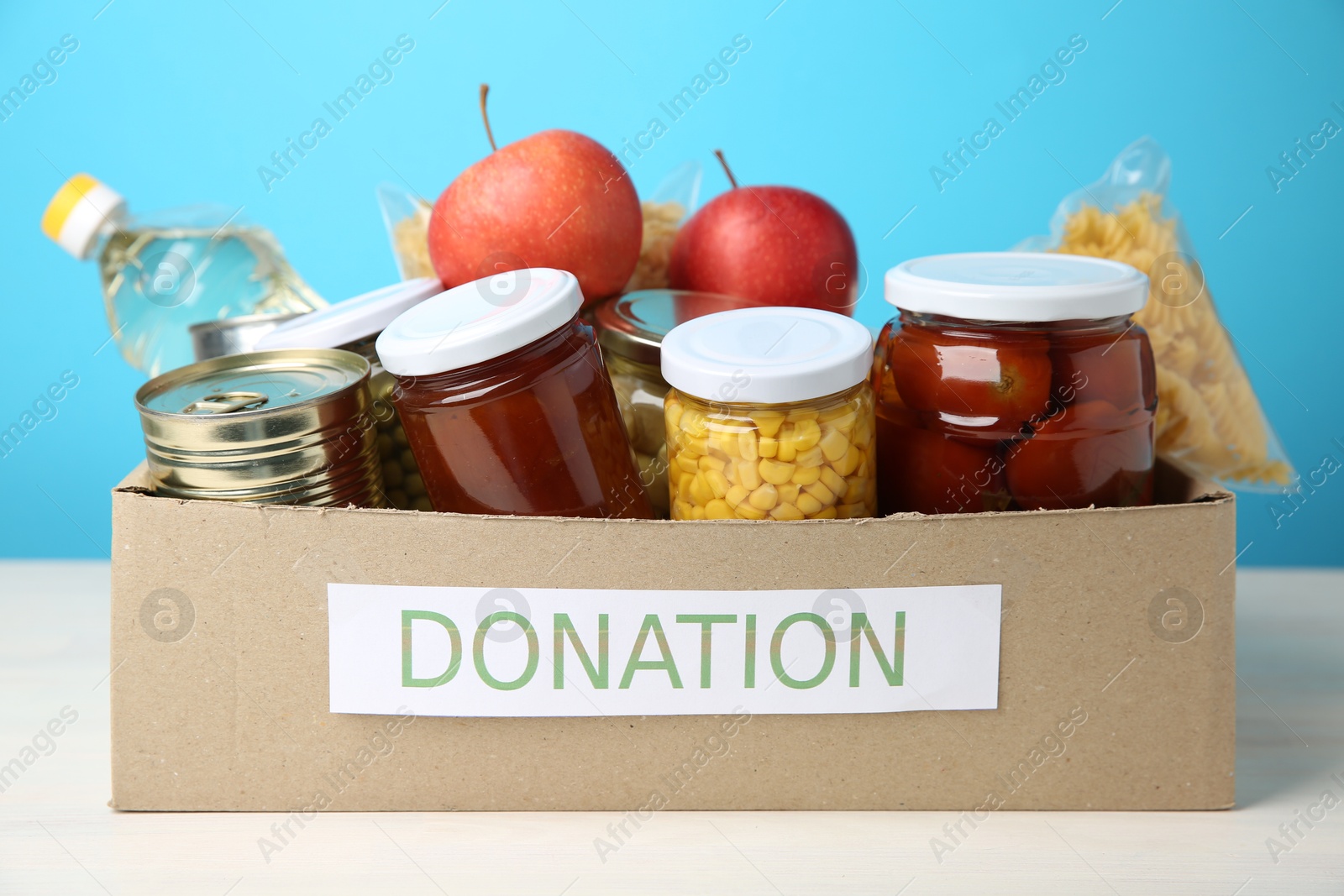 Photo of Different food products for donation in box on table against light blue background