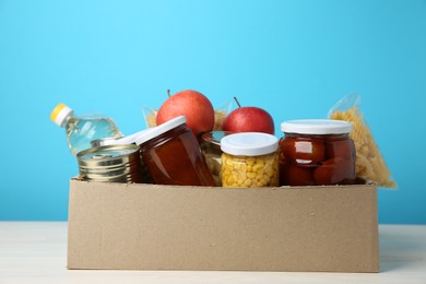 Photo of Different food products for donation in box on table against light blue background