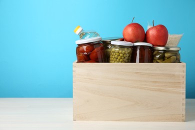 Photo of Different food products for donation in wooden crate on table against light blue background, space for text