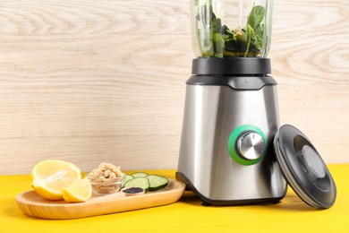 Photo of Modern blender with ingredients for smoothie on yellow wooden table. Space for text