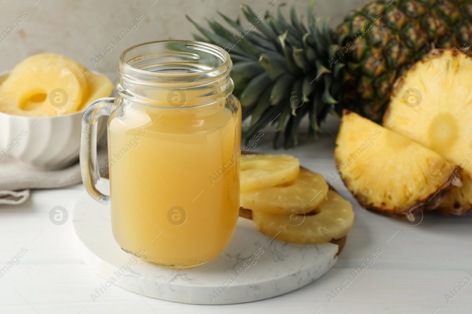 Photo of Tasty pineapple juice in mason jar and fresh fruits on white wooden table against grey background, closeup