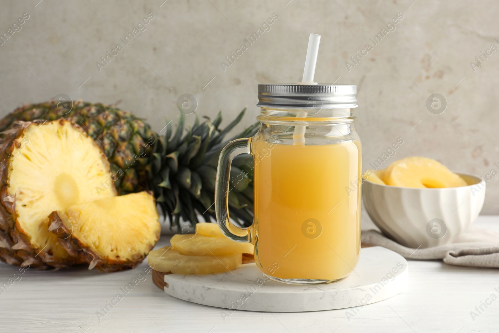 Photo of Tasty pineapple juice in mason jar and fresh fruits on white wooden table against grey background, closeup