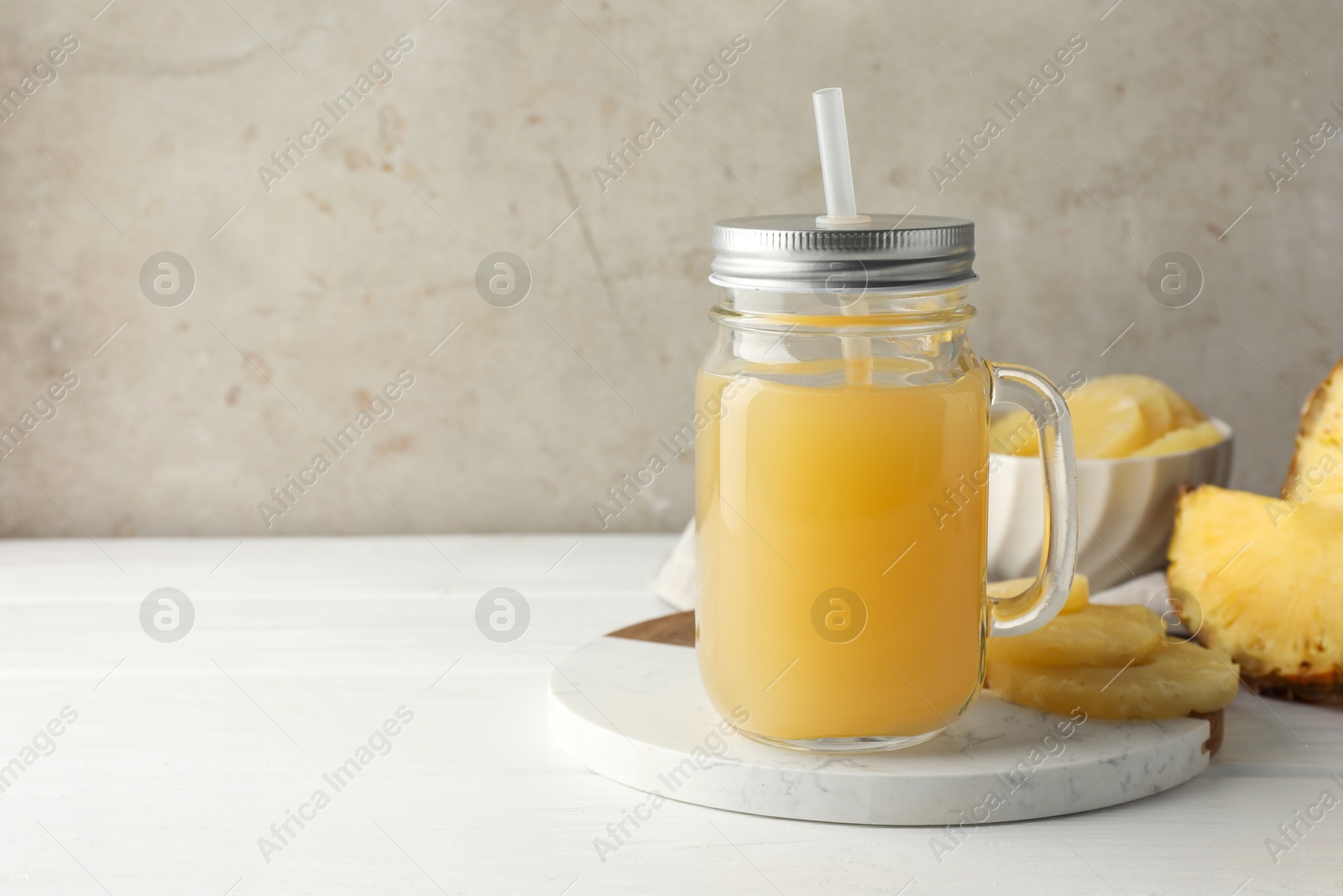 Photo of Tasty pineapple juice in mason jar and slices of fresh fruit on white wooden table against grey background, closeup. Space for text