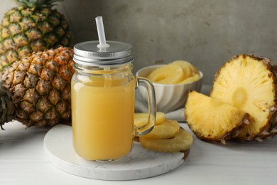 Photo of Tasty pineapple juice in mason jar and fresh fruits on white wooden table against grey background, closeup