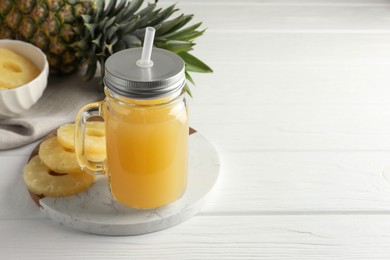 Photo of Tasty pineapple juice in mason jar and slices of fresh fruit on white wooden table, closeup. Space for text