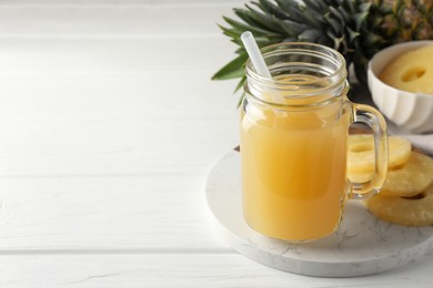 Photo of Tasty pineapple juice in mason jar and slices of fresh fruit on white wooden table, closeup. Space for text