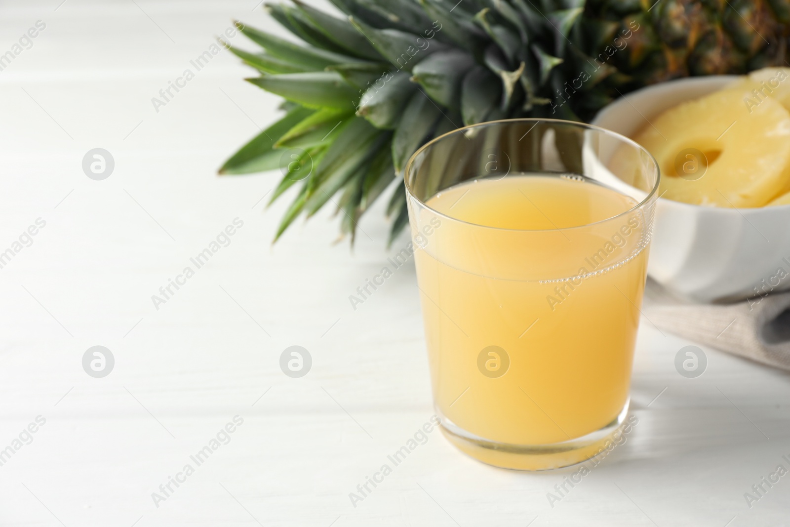 Photo of Tasty pineapple juice in glass and fresh fruit on white wooden table, closeup. Space for text