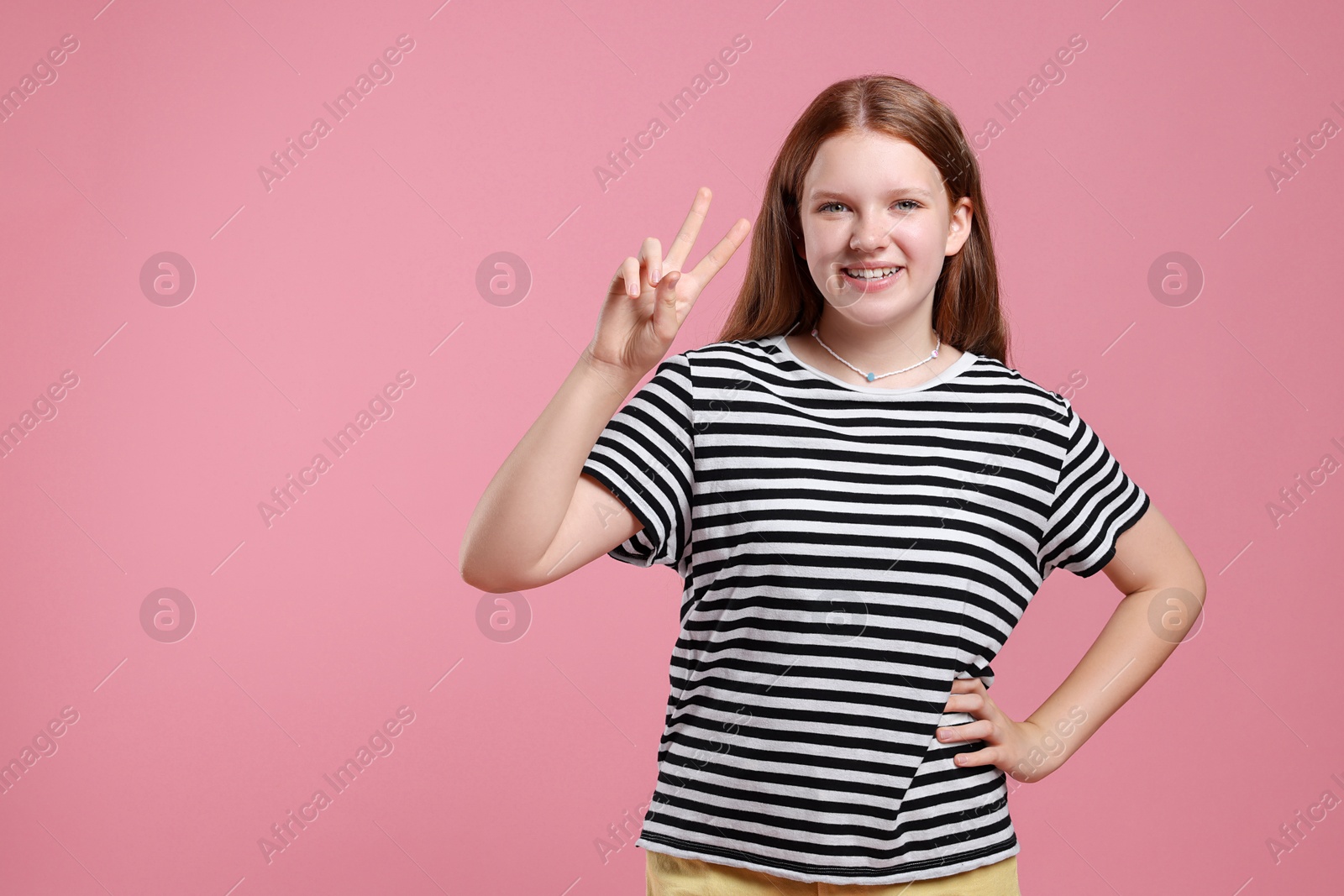 Photo of Teenage girl with showing v-sign on pink background, space for text